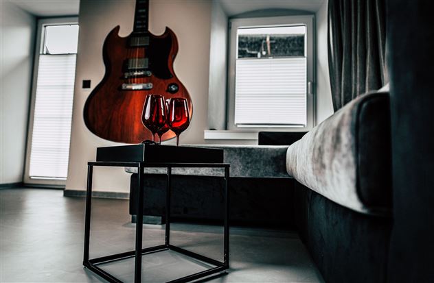 A modern living room with an electric guitar on the wall. On a table, there are two wine glasses.