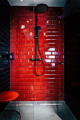 Eine moderne Dusche mit roten Fliesen und einer schwarzen Rainshower-Dusche. Ein kleiner roter Hocker steht neben der Dusche.