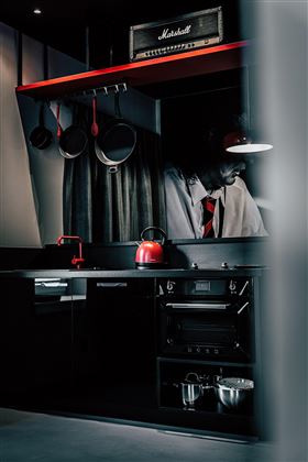 A modern kitchen with black design and red accents. On the countertop, there are pots and a red tea or coffee pot.