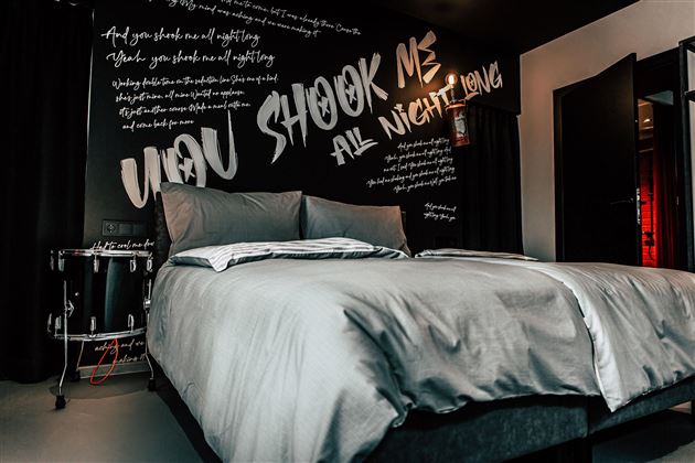 Ein modernes Schlafzimmer mit einem großen Bett und einer stilvollen Wandgestaltung. Die Wand ist mit auffälligen Texten in verschiedenen Schriftarten verziert.