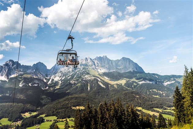 A cable car travels over the impressive mountains and valleys. The sky is blue with some clouds.