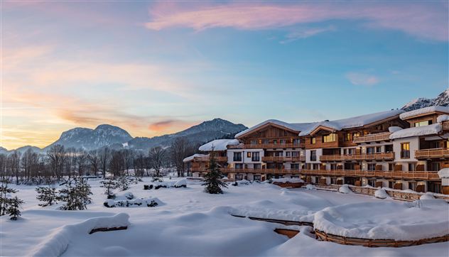 A beautiful hotel in a snowy landscape. The mountains are in the background and the sky shines in soft colors.