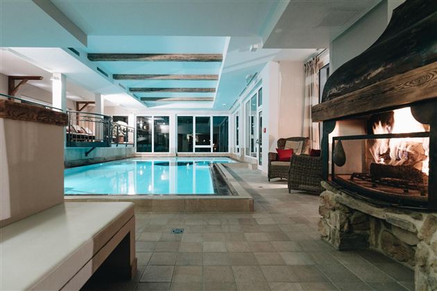 An elegant indoor pool with smooth water and modern lighting elements. Next to the pool, there is a cozy fireplace that creates a warm atmosphere.