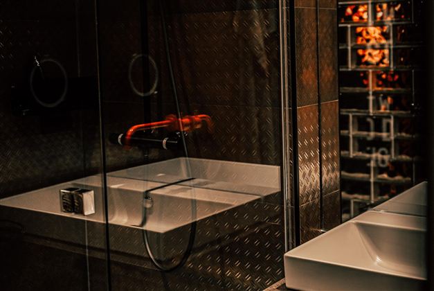A modern bathroom with an elegant shower and a white bathtub. The walls are made of dark material, creating a stylish atmosphere.