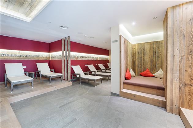 A modern relaxation room with comfortable loungers and wooden details. The walls are painted in warm shades of red, creating an inviting atmosphere.