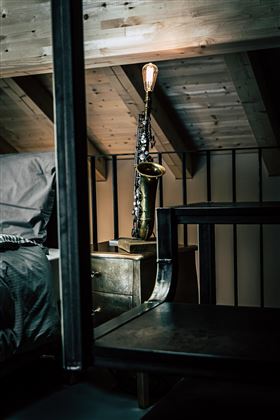 Ein stilvolles Schlafzimmer mit einem Bett und einem Nachttisch. Auf dem Nachttisch steht eine dekorative Saxophonlampe.