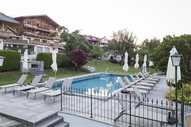 A beautiful outdoor area with a pool and loungers. The surroundings are green and well-maintained, perfect for relaxing.