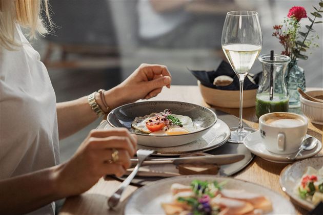 An elegant breakfast with a plate that contains eggs and vegetables. Next to it is a glass of wine and a cup of coffee.