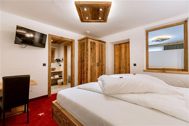 A modern bedroom with a large bed and wooden furniture. The room has a television and a pleasant atmosphere.