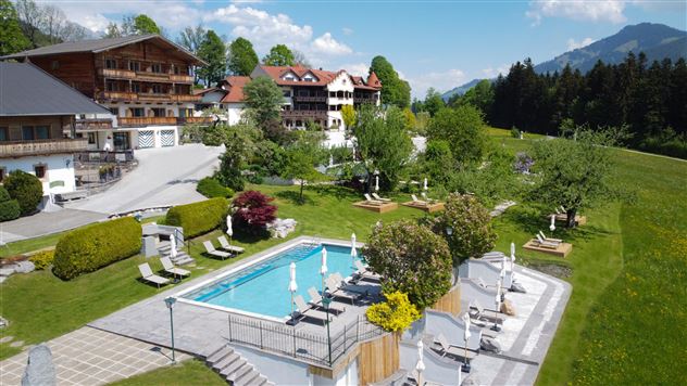 A beautiful outdoor area with a pool and loungers. In the background, picturesque mountains and green meadows can be seen.