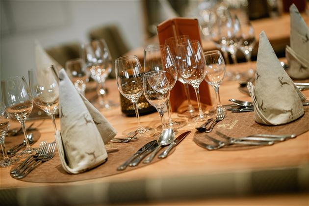 An elegantly set table with cutlery, glasses, and decorated napkins. The warm wood look creates an inviting atmosphere.