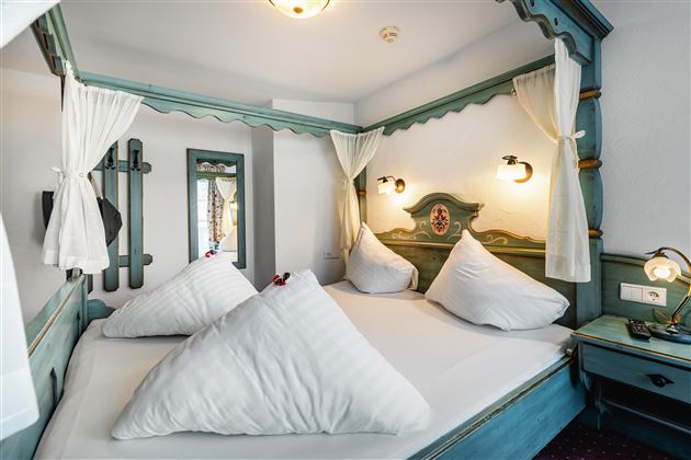 A cozy bedroom with a large bed and three decorative pillows. The beautiful walls and warm lights create an inviting atmosphere.