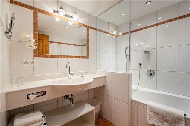 A modern bathroom with a shower and a bathtub. The white tiles and the good lighting create a bright atmosphere.