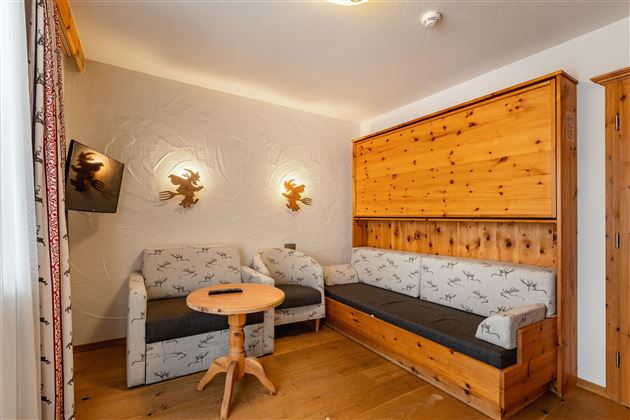 A cozy living room with wood paneling and a sofa. A round table and a television are also present.