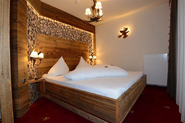 A cozy bedroom with a wooden bed and decorative pillows. The warm light accents and the wooden paneling create an inviting atmosphere.