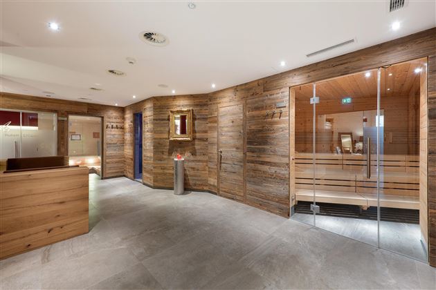 A modern wellness area with wooden walls and soft lighting. The sauna and reception areas are designed to be clear and inviting.