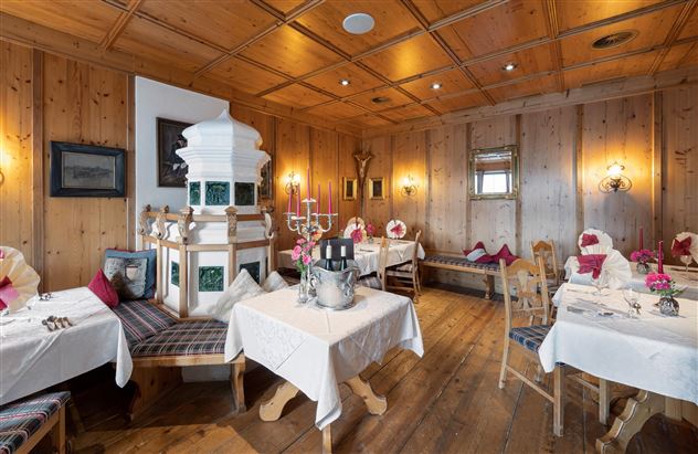 A cozy restaurant with wooden walls and elegantly set tables. In the center stands a traditional tiled stove.