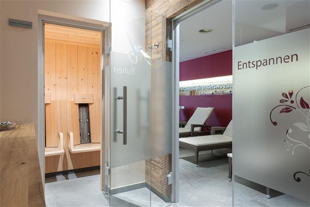 A modern wellness area with glass doors. On the left side, there is a sauna, while the room on the right invites you to relax.