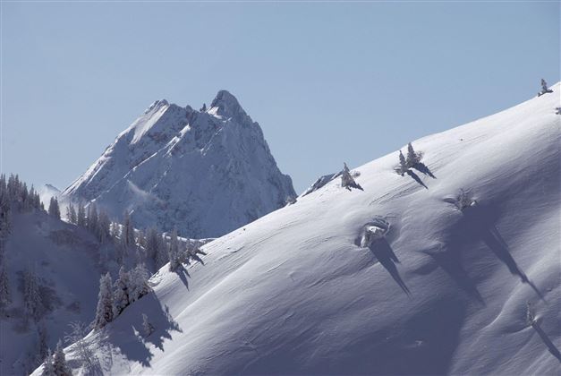 A snow-covered mountain landscape with a high peak in the background. The sky is clear and blue, creating a tranquil atmosphere.