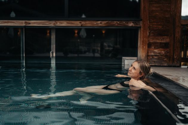 A woman relaxes in the water of a wellness pool. The room is designed to be modern and cozy.