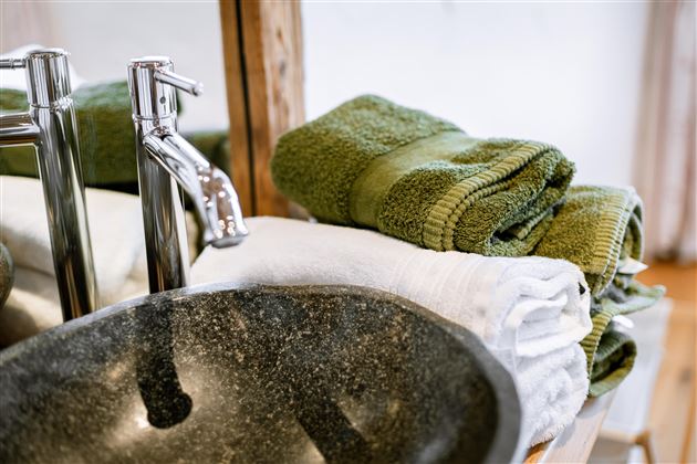 A modern stone sink with shiny faucets. On it lie clean, green, and white towels.