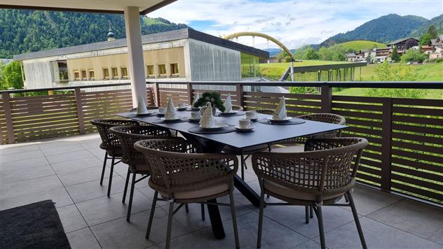 A tastefully furnished dining table on a terrace with a view of green hills and mountains. The space is bright and inviting, perfect for sociable meals outdoors.