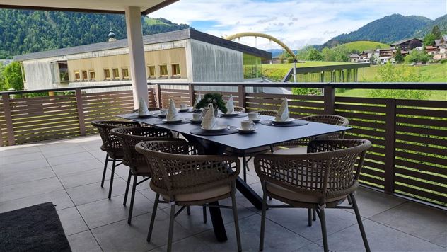 A cozy dining area on a terrace with a view of the mountains. The table is set for guests and offers a beautiful view of the landscape.