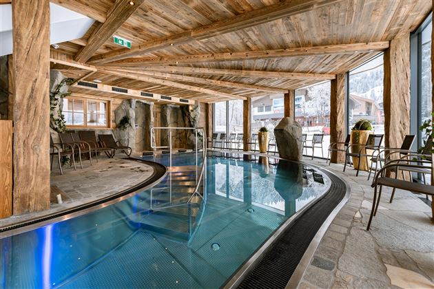 An elegant indoor pool in a wooden-decorated room. The light gently falls through the windows, creating a relaxing atmosphere.