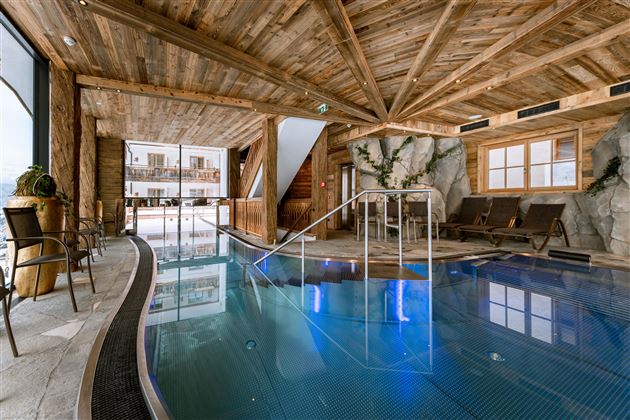 An elegant indoor pool in a wooden building with large windows. Comfortable loungers and natural elements create a relaxing atmosphere.
