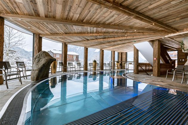 An elegant indoor pool in a rustic wooden building. Large windows offer a view of the snow-capped mountains.