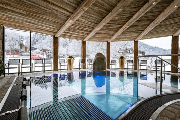 An indoor pool in a wooden cabin with large windows overlooking snow-covered mountains. Relaxation and tranquility in a cozy atmosphere.