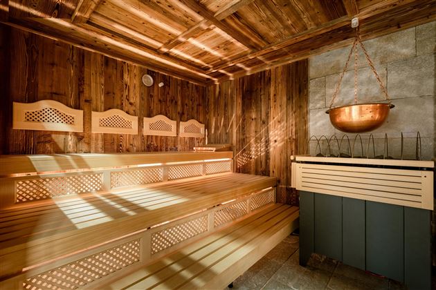 A quiet sauna with a wooden bench and warm light. The walls are clad in wood and a copper bowl hangs from the ceiling.