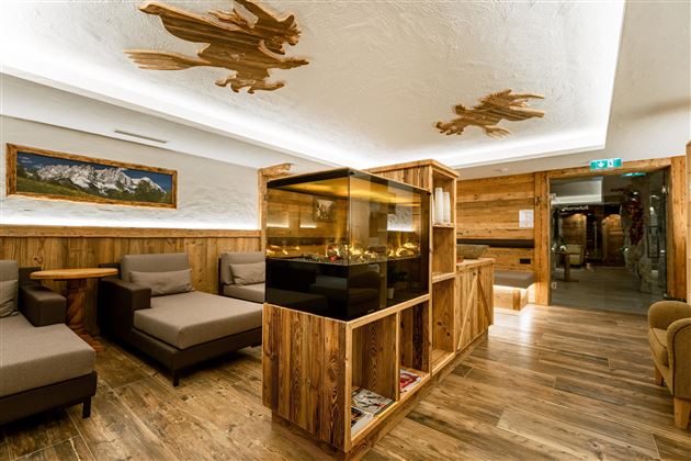 A cozy room with wooden furniture and a central aquarium. Ceiling decorations and warm lighting create an inviting atmosphere.