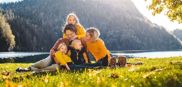 A family is sitting on a meadow by the shore of a lake. They are wearing cheerful yellow clothing and enjoying a sunny day in nature.