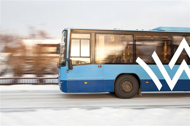 A blue bus is driving quickly on a snow-covered road. In the background, blurry trees are visible.