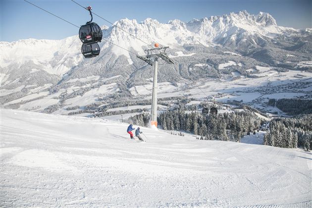 A beautiful winter landscape with snow-covered mountains. Skiers enjoy the descent under a cable car.
