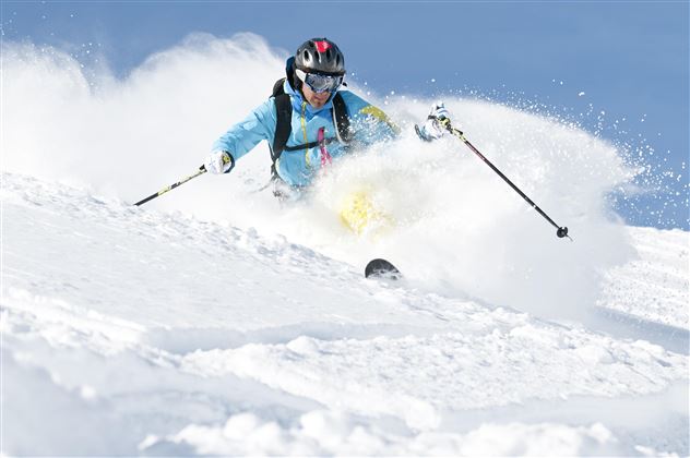 A skier glides through fresh snow in the mountains. The sky is clear and blue, perfect for a fantastic ski day.