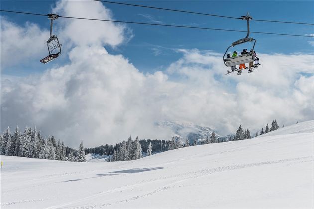A snowy landscape with a ski lift and clouds in the background. The trees are covered in snow, and there is a clear, cold atmosphere.