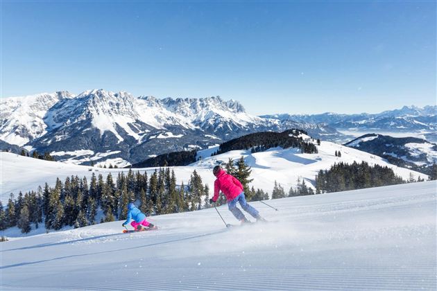 A beautiful winter sports area with snow-covered slopes and mountains in the background. Two skiers enjoy the sun and the fresh air.