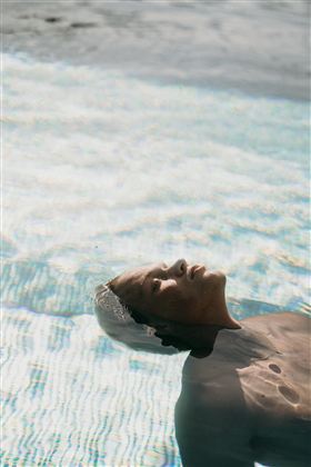 A man is lying relaxed on the water in a pool. The gentle waves reflect the light and create a calm atmosphere.