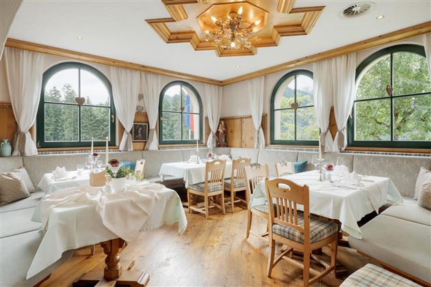 A cozy restaurant with wooden decor and large windows offering views of greenery. Tables are festively set and invite guests to linger.