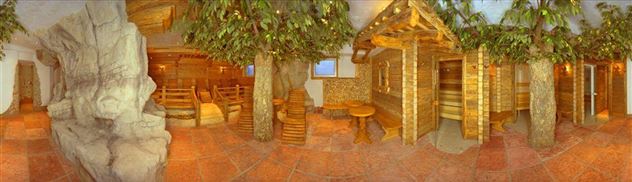 A cozy wellness area with wooden saunas and a green plant flair. The floor is made of red stone tiles, creating a relaxing atmosphere.