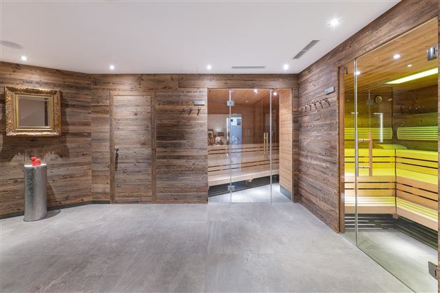 A modern wellness area with wooden paneling and gentle light sources. In the background, a sauna is visible through glass doors.