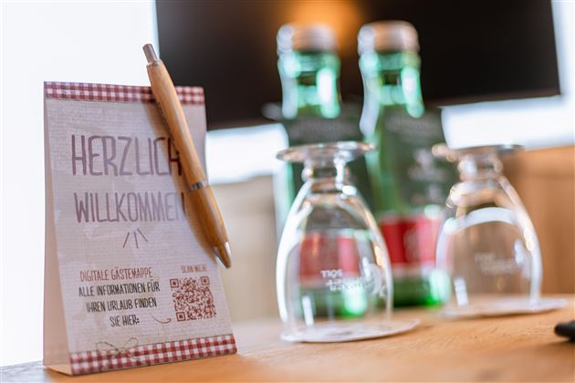 A welcome text on a table with a pen and glasses. Bottles of water are visible in the background.