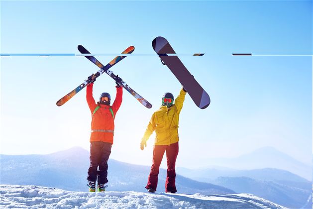 Zwei Wintersportler stehen auf einem schneebedeckten Berg. Einer hält Skier, der andere ein Snowboard hoch in die Luft.