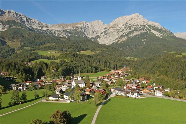 A picturesque mountain landscape with a small town in the valley. The surroundings are green and surrounded by majestic mountains.