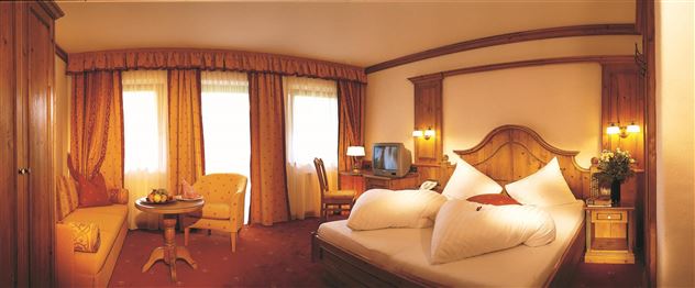 A cozy hotel room with a large bed and colorful curtains. There is a seating area with a table and a television in the room.