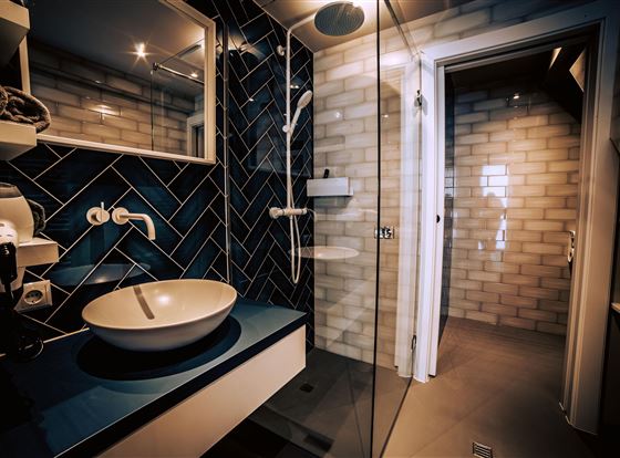 Een moderne badkamer met blauwe tegels en een elegante douche. Het wastafel is ovaal en stijlvol geplaatst op een witte console.