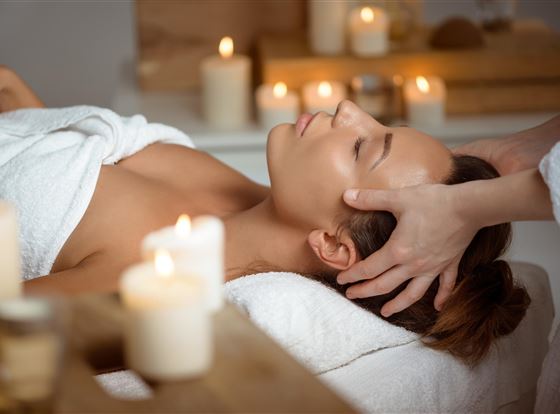 Una aplicación de bienestar relajante con una mujer recibiendo un masaje en la cabeza. A su alrededor se ven velas y un ambiente tranquilo.