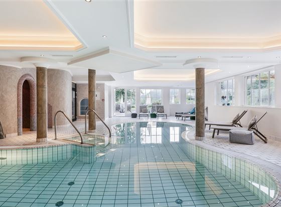 Ein luxuriöser Innenpool mit glattem, grünem Fliesenboden. Die Umgebung ist hell und modern, mit großen Fenstern und bequemen Liegen.
